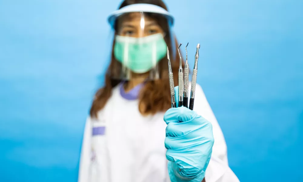 Frau in medizinischer Schutzkleidung hält zahnmedizinische Werkzeuge in die Kamera